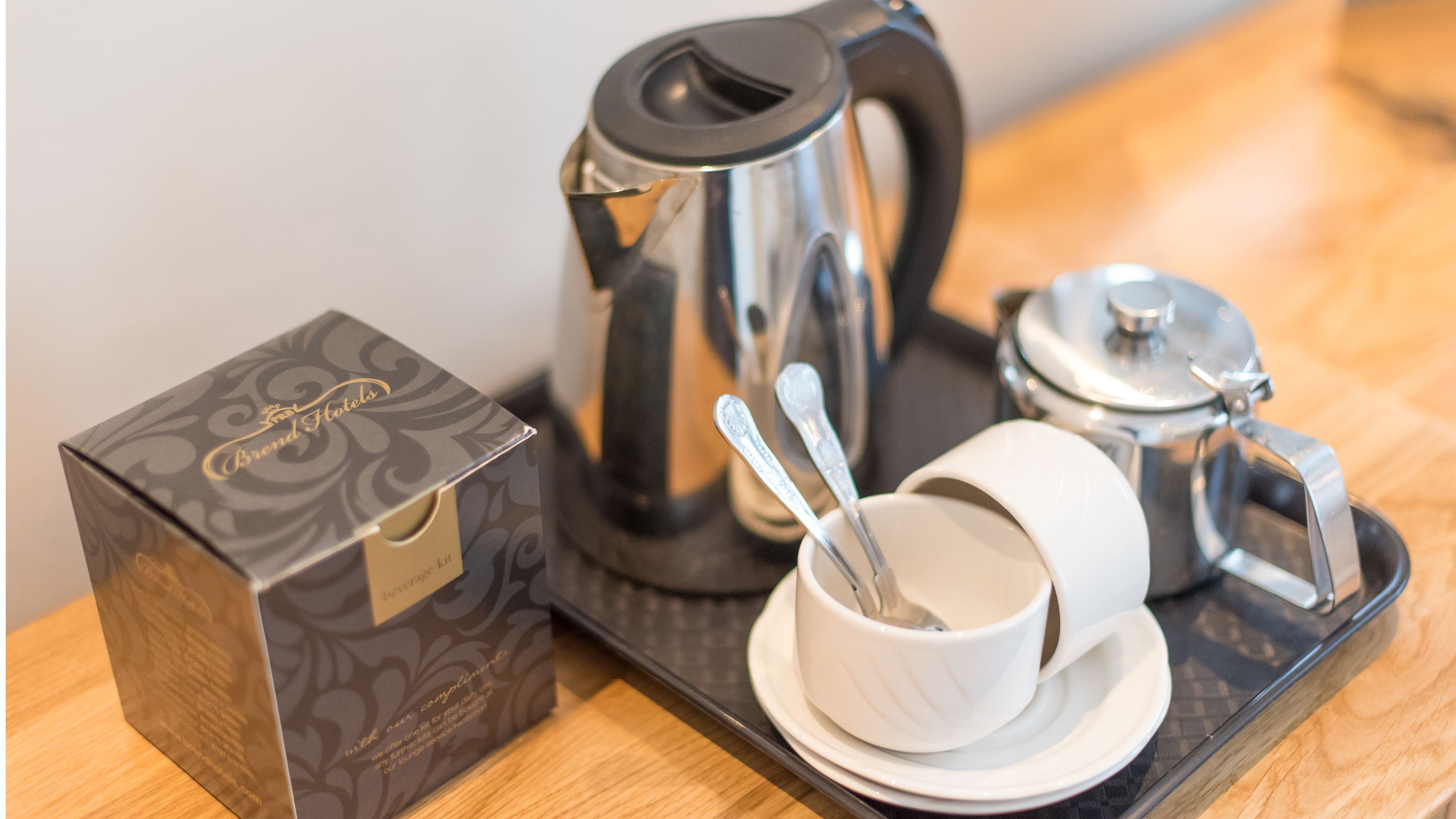 A coffee maker, a cup with a spoon, and a box on a tray.