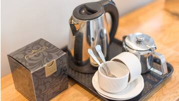 A coffee maker, a cup with a spoon, and a box on a tray.
