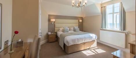 A bedroom with a large bed, bedside lamps, a nightstand, a dresser, a mirror, and a window with curtains.