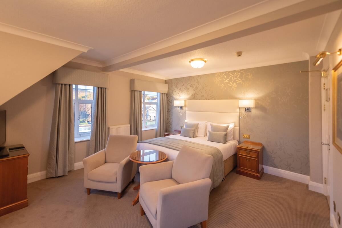 Ein Hotelzimmer mit einem großen Bett, zwei Sessel, einem kleinen runden Tisch und einem Nachttisch.