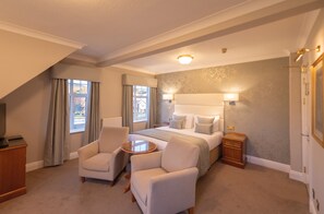 Una habitación de hotel con una cama grande, dos sillones, una mesita redonda y una mesita de noche.