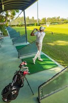 Un campo de golf con un tee, un golfista en pleno swing y un bolso de golf en el suelo.
