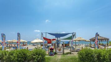 Una playa con sombrillas, sillas de descanso y una zona de juegos para niños.