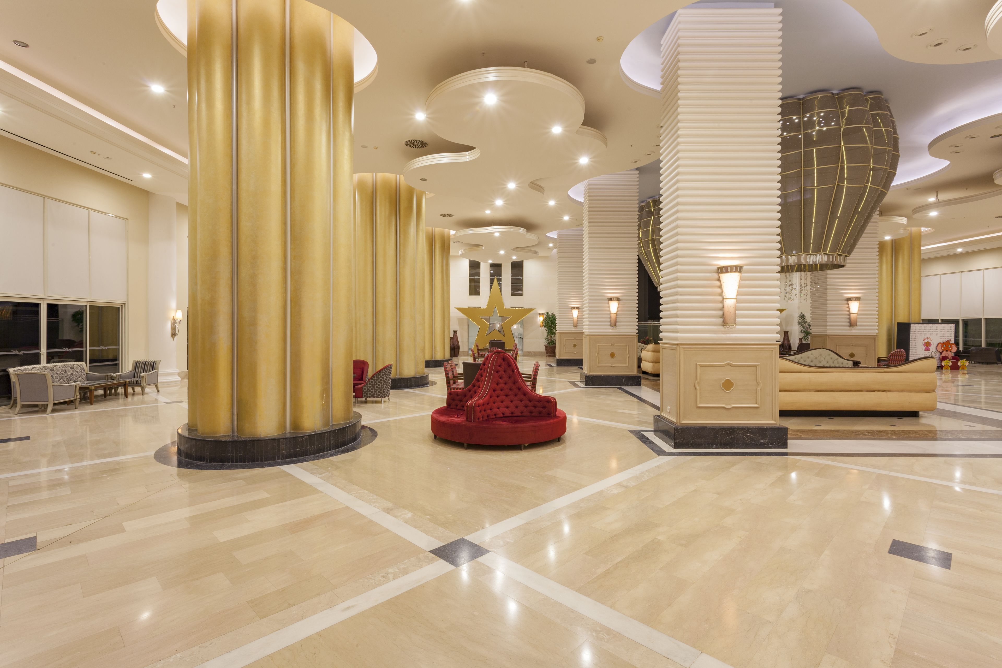 A spacious lobby with high ceilings, large golden pillars, and a central red seating area.