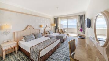 Habitación de hotel con dos camas, un escritorio, una silla, un televisor y un ventanal con vistas al mar.