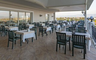 Un restaurante con terraza, mesas con manteles blancos y sillas.