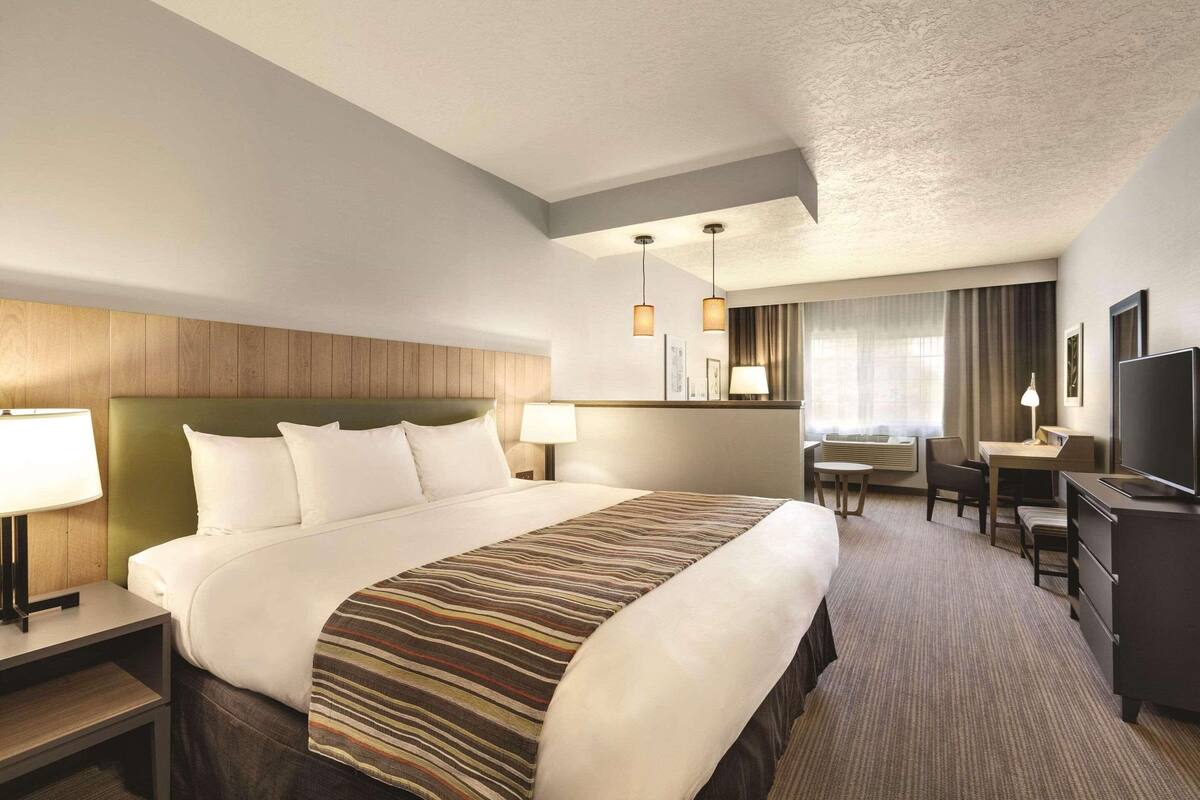 A hotel room with a large bed, a desk, a chair, a TV, and a lamp.