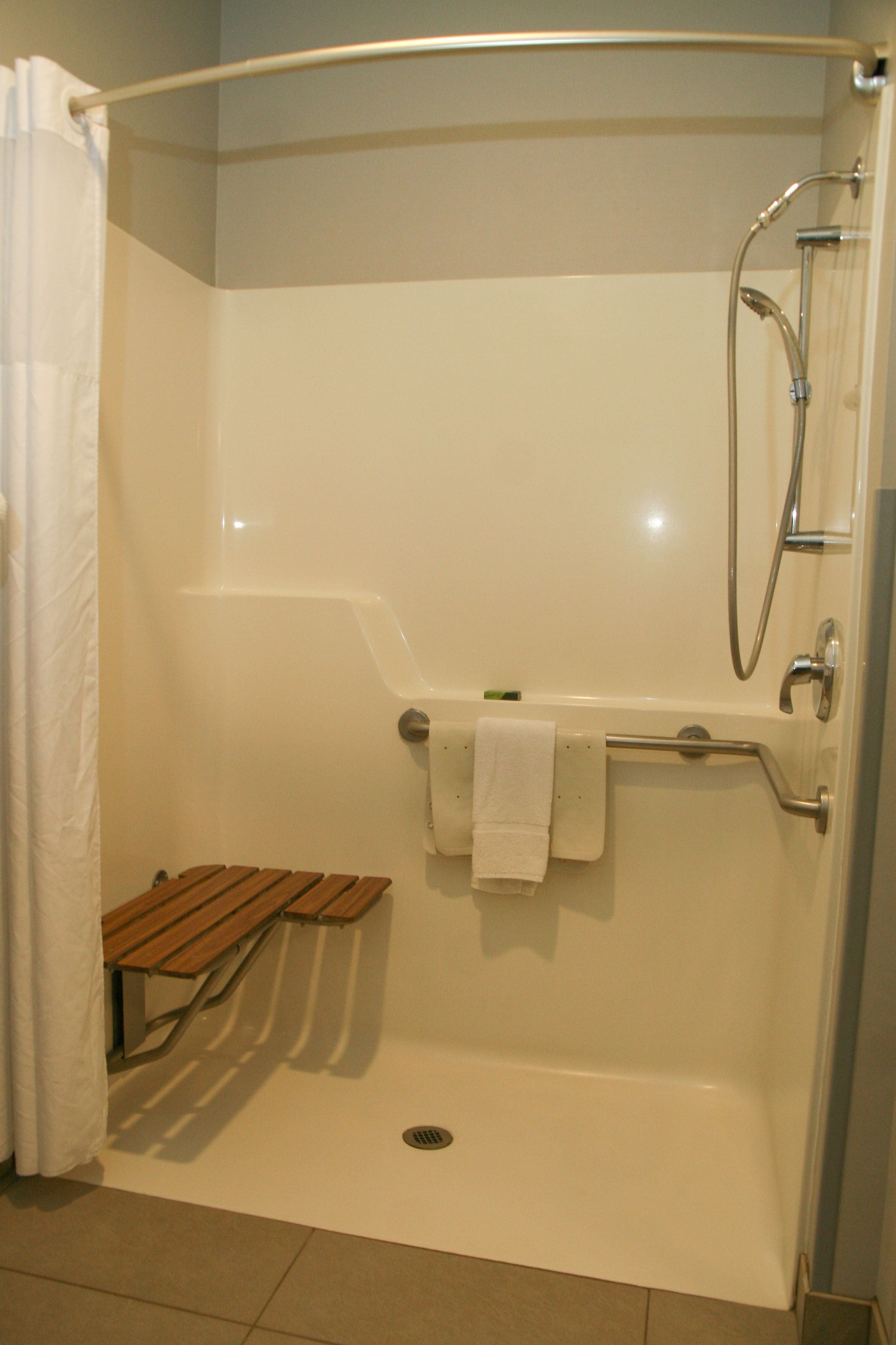 A shower area with a glass door, a wooden bench, and a towel rack.