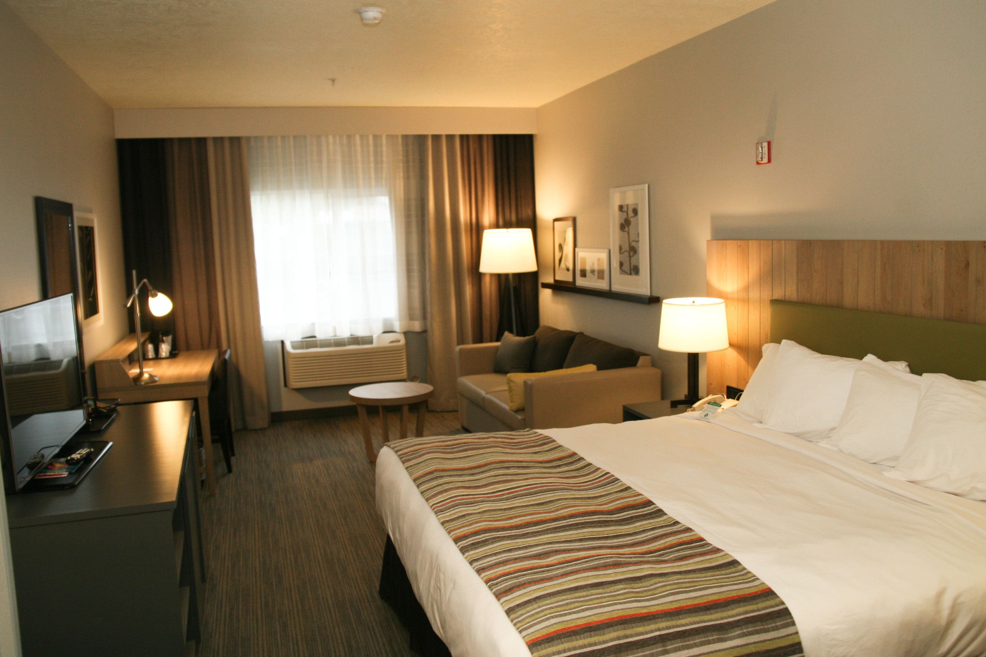A hotel room with a bed, a desk, a chair, a sofa, and a lamp.
