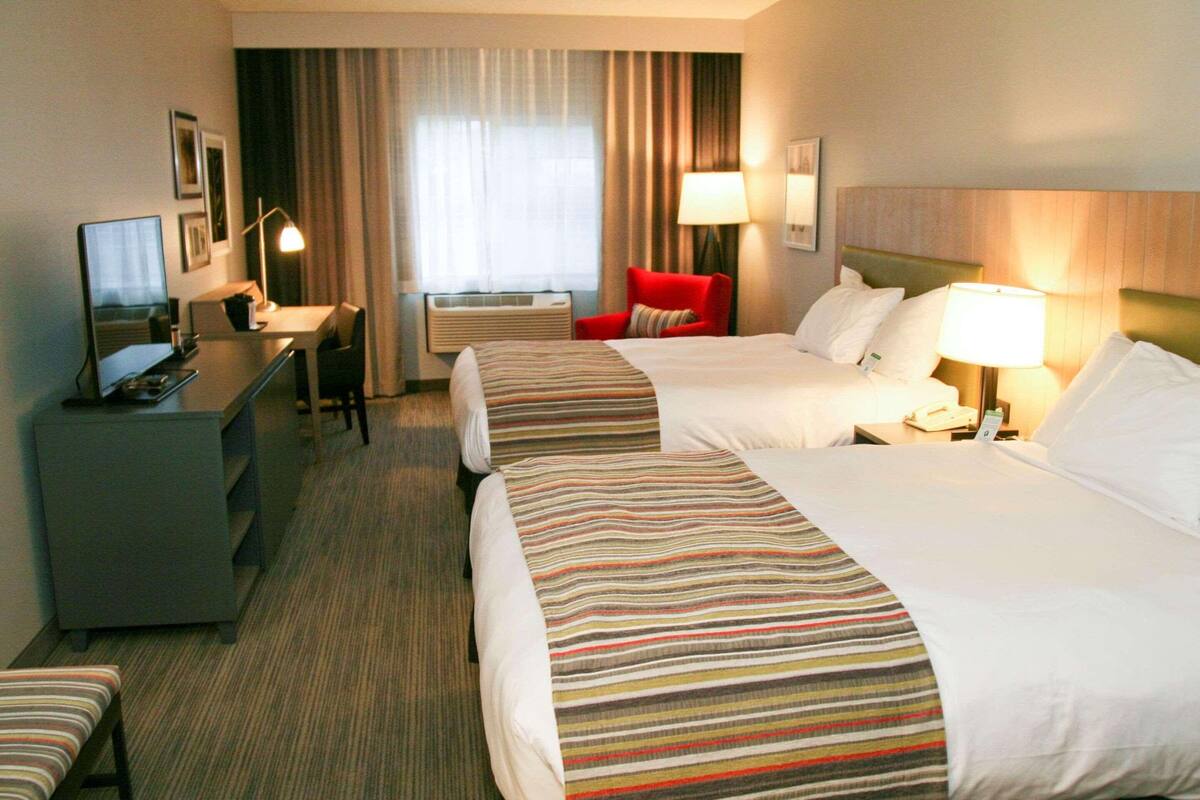 A hotel room with two beds, a desk, a chair, a TV, and a window with curtains.