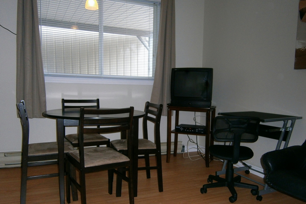 Ein Zimmer mit Esstisch, Stühlen, einem Fernseher und einem Computertisch.