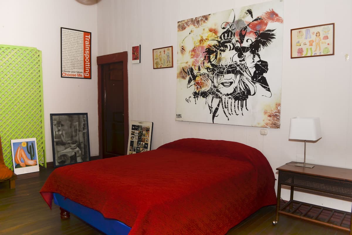 Ein Zimmer mit rotem Bettbezug, einer Wand mit verschiedenen Kunstwerken und einer Wand mit grünem Muster.