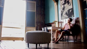 Una habitación con un ventanal grande, una silla, una mesa y un cuadro en la pared.