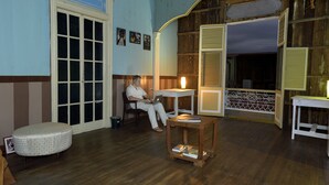 Una habitación con piso de madera, un otoman redondo, una mesa con una computadora portátil y una silla.