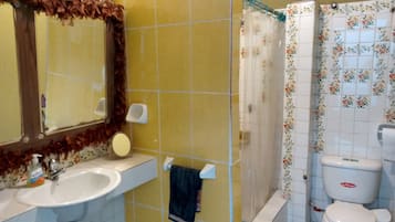 A bathroom with yellow tiles, a white sink, a mirror, a shower curtain, and a toilet.