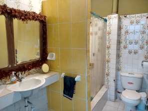 Une salle de bain avec des carreaux jaunes, un lavabo blanc, un miroir, un rideau de douche et des toilettes.