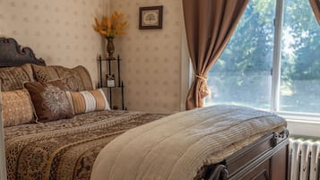 A bedroom with a large bed, a radiator, a window with curtains, and a wall-mounted picture.