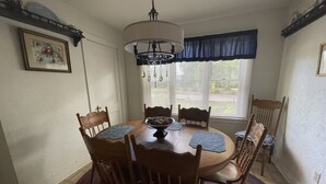 Un comedor con una mesa redonda de madera, seis sillas, una araña y una ventana con persianas.