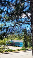 Un edificio azul con un espacio al aire libre techado, rodeado de árboles y un estacionamiento.