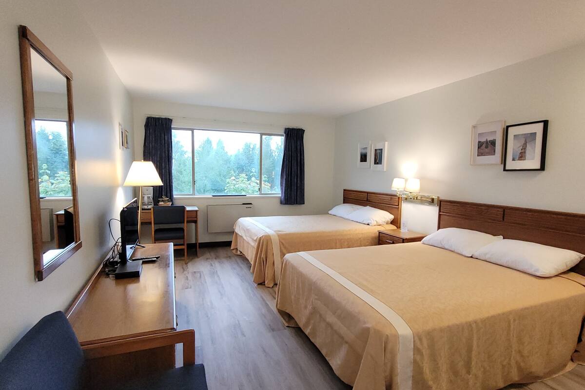 A hotel room with two beds, a desk, a chair, a lamp, and a large window with curtains.