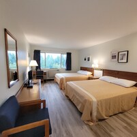 Habitación de hotel con dos camas, un escritorio, una silla, una lámpara y un ventanal grande con cortinas.