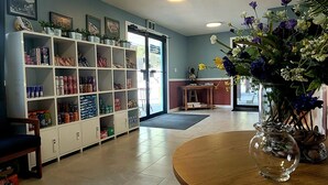 A room with a tiled floor, a wooden table with a vase of flowers, and a shelving unit with various items. - Ridgeview Motor Inn (Gold River)