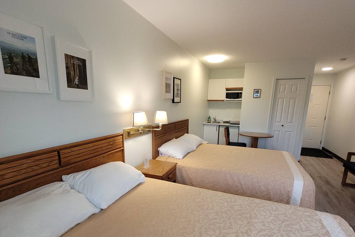 A hotel room with two beds, a small kitchenette, and a door leading to another room.