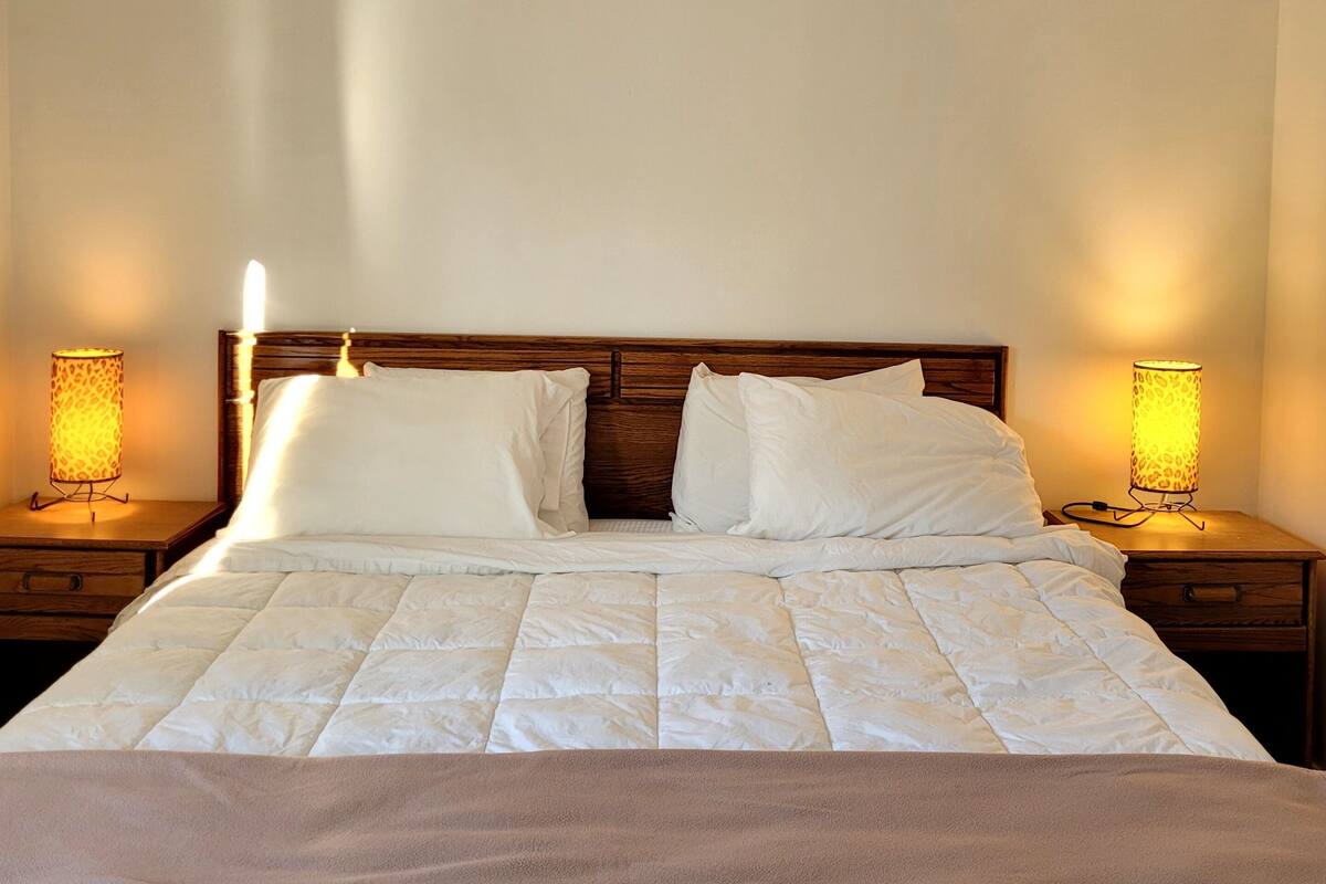 A neatly made bed with a brown blanket, two bedside lamps, and a wooden headboard.