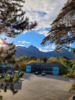 Un estacionamiento con un edificio al fondo, rodeado de árboles y montañas.