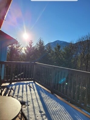 A balcony with a table and chairs, overlooking a mountainous landscape with trees and a clear sky.