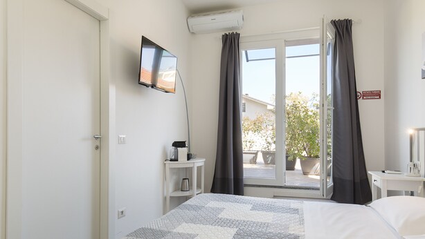 A hotel room with a bed, a TV mounted on the wall, a small table with a kettle, and a window with curtains. - B&B La Terrazza (Rho)