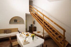 A dining area with a wooden staircase, a sofa, and a small table set with breakfast. - Appartamenti la Principina - I Casali (Grosseto)