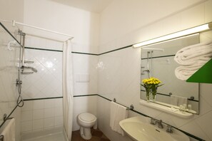 A bathroom with a glass shower enclosure, a toilet, a sink, and a mirror with a towel rack. - Appartamenti la Principina - I Casali (Grosseto)