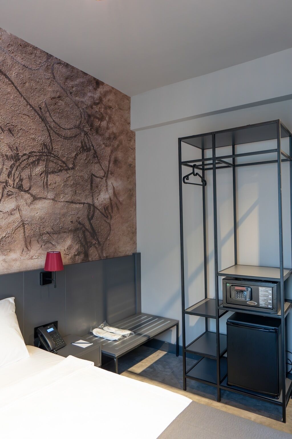 Una habitación de hotel moderna con una cama grande, un escritorio con una computadora, un teléfono y una lámpara roja montada en la pared.