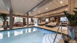 A spacious indoor pool area with multiple seating options, including a large sofa and chairs, surrounded by large windows and potted plants. - Romantik Hotel & Restaurant Stafler (Campo di Trens)