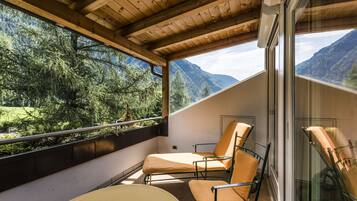 A balcony with two lounge chairs, a glass door, and a view of a mountainous landscape.