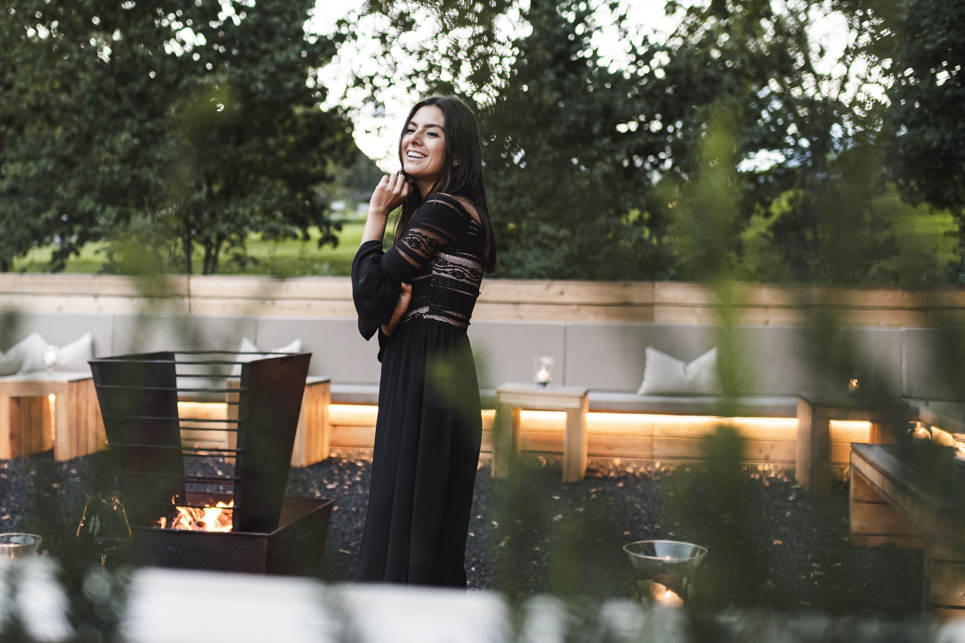 A person standing near a fire pit with seating and a wooden bench in a garden setting.