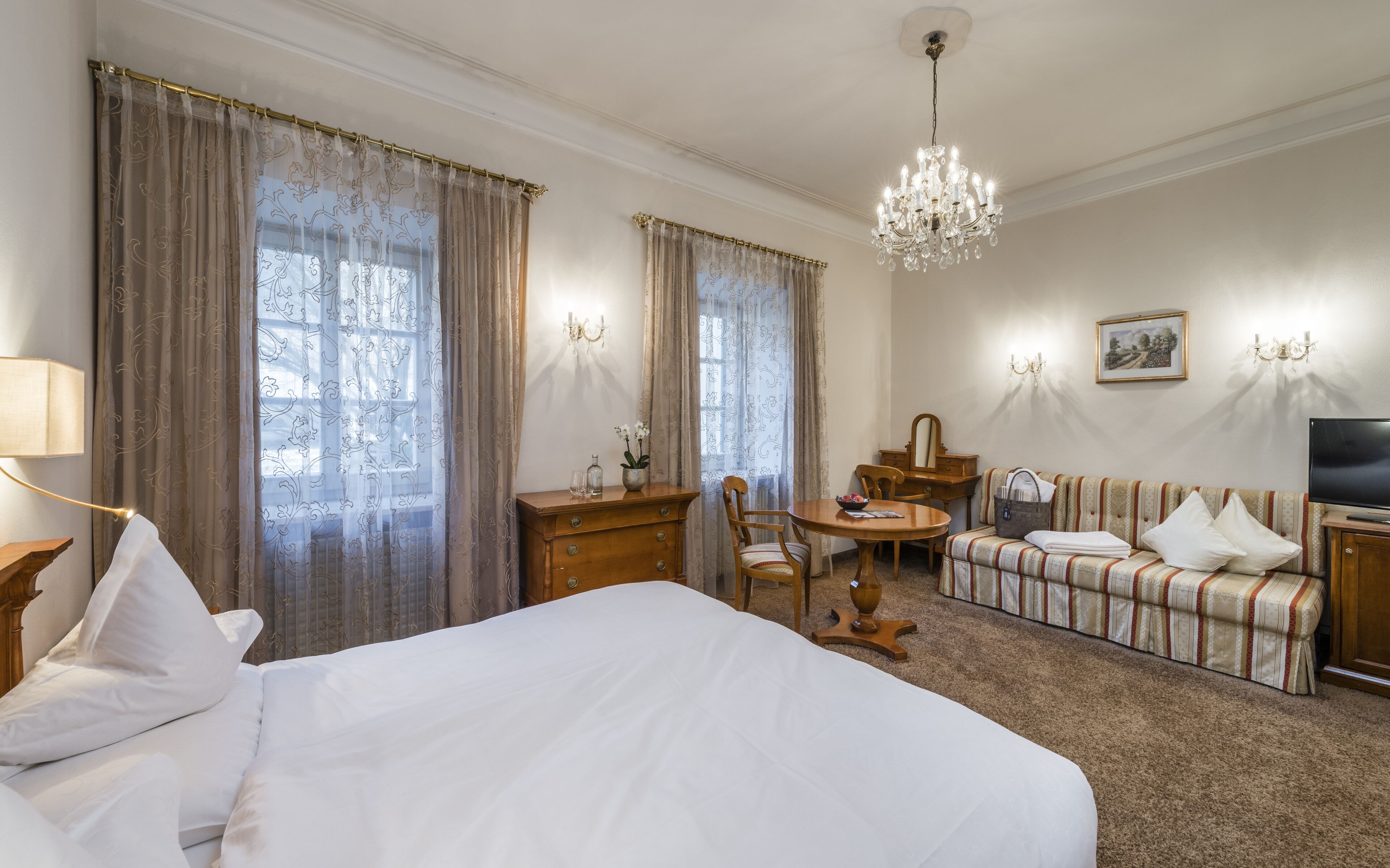 A hotel room with a large bed, a wooden desk, a small round table, a sofa, and a television.