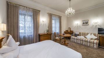 A hotel room with a large bed, a wooden desk, a small round table, a sofa, and a television.