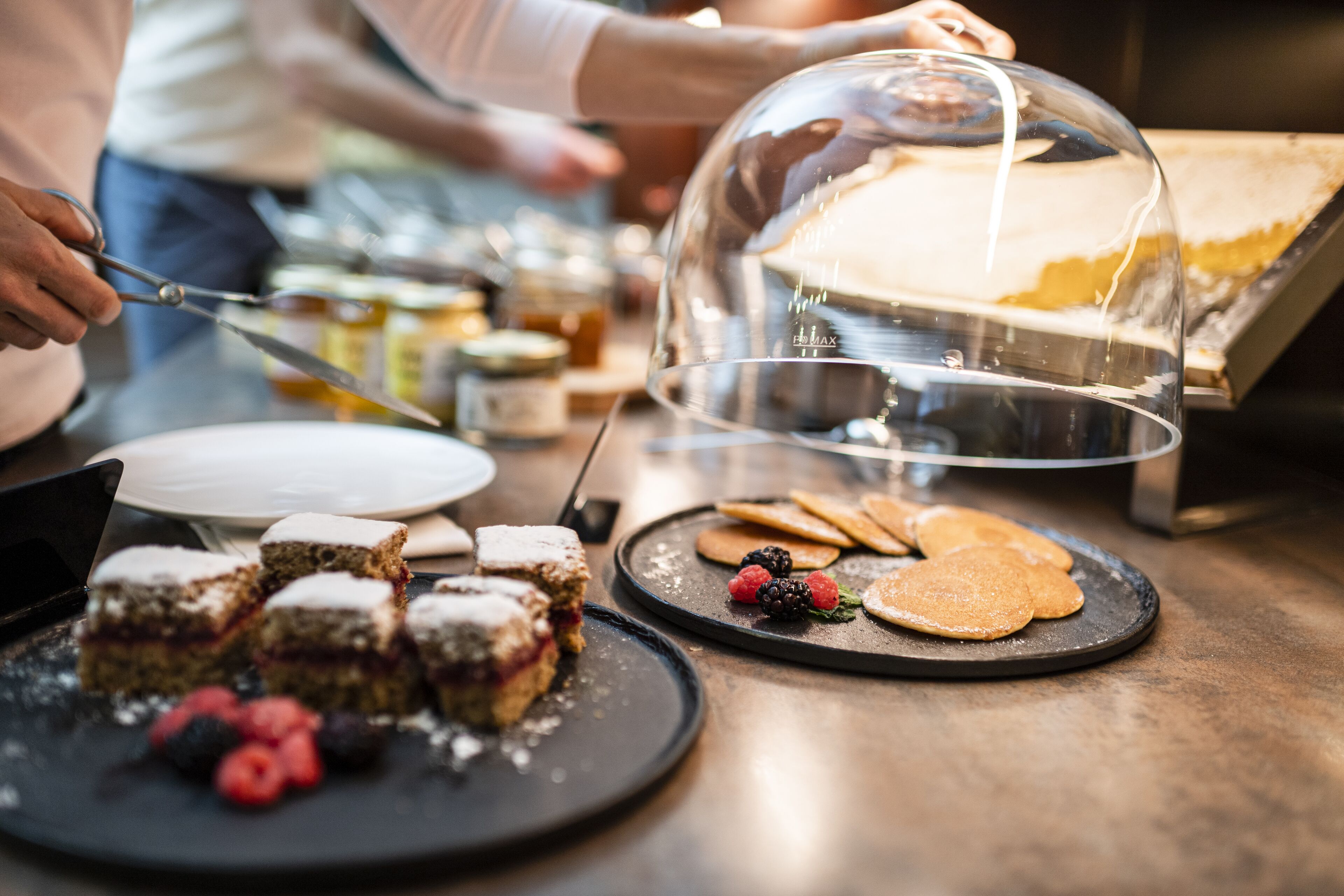 A dessert display with various pastries and fruits, including a cake under a glass dome.