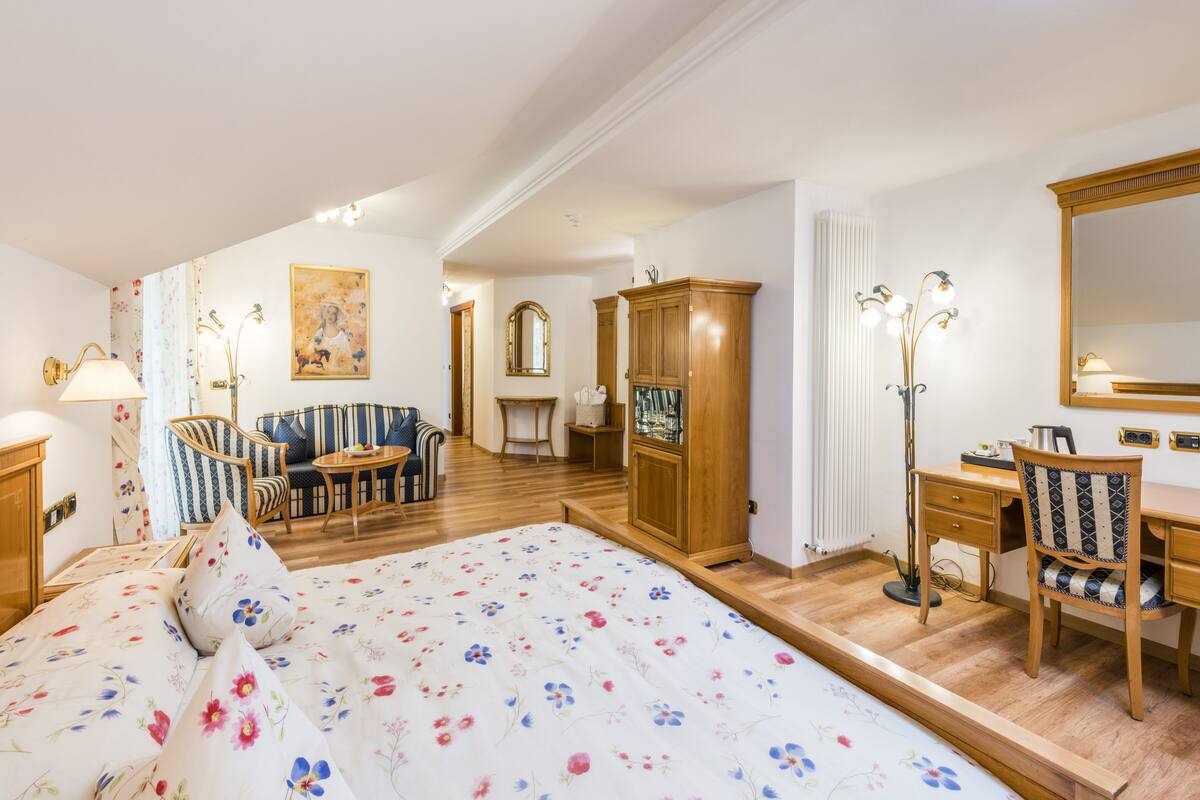 A hotel room with a large bed, a sofa, a desk, a chair, a cabinet, and a mirror.