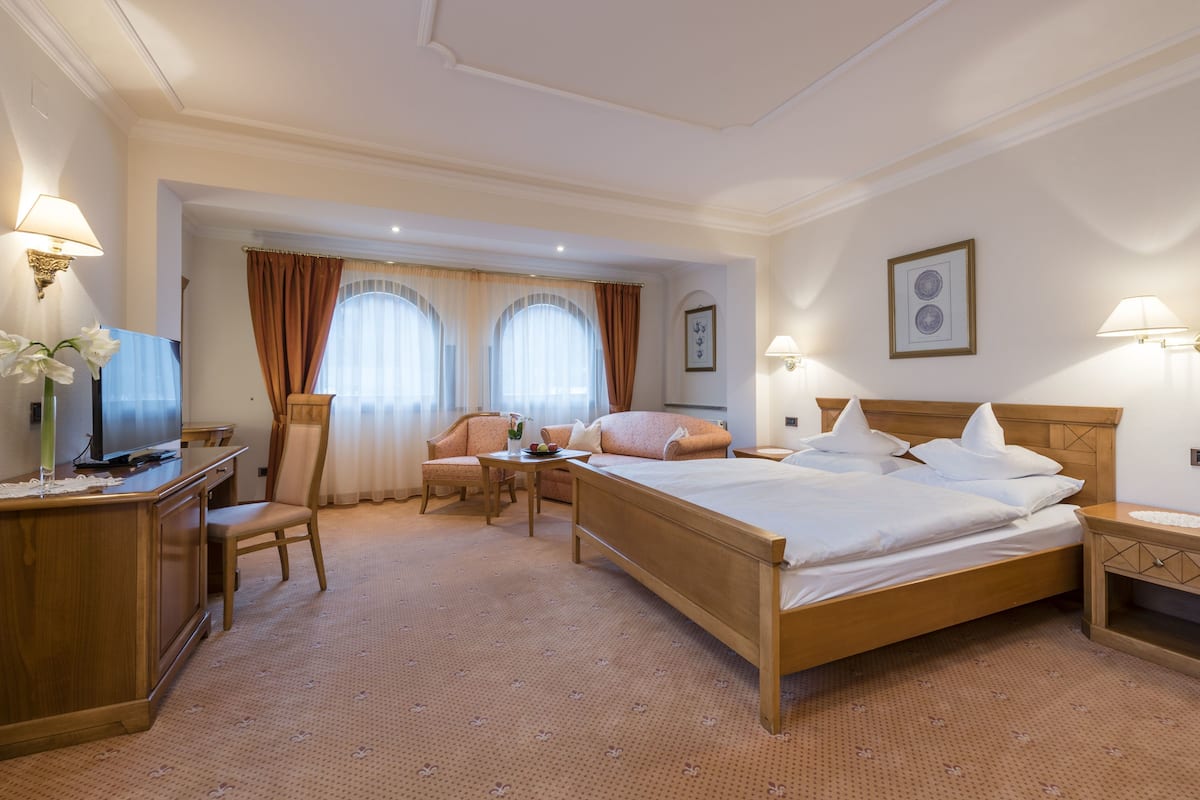 A hotel room with a bed, a desk with a television, a chair, and a small table with a vase of flowers.