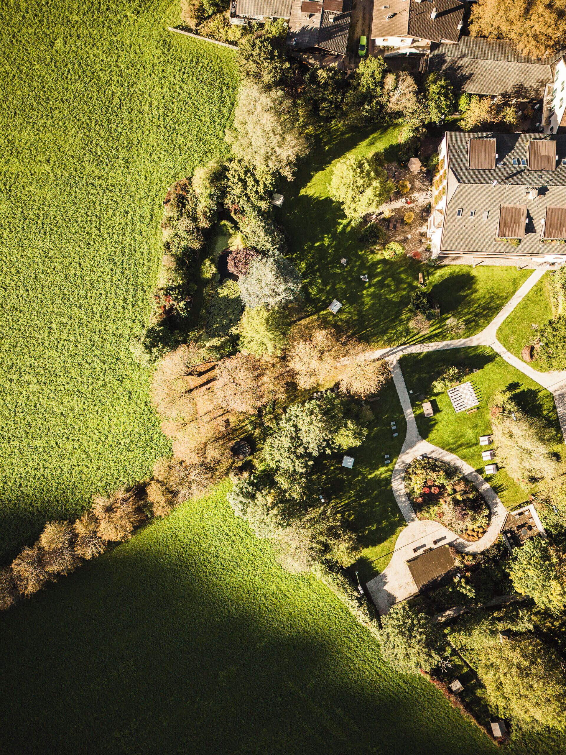 An aerial view of a residential area with a house, green fields, and a garden.