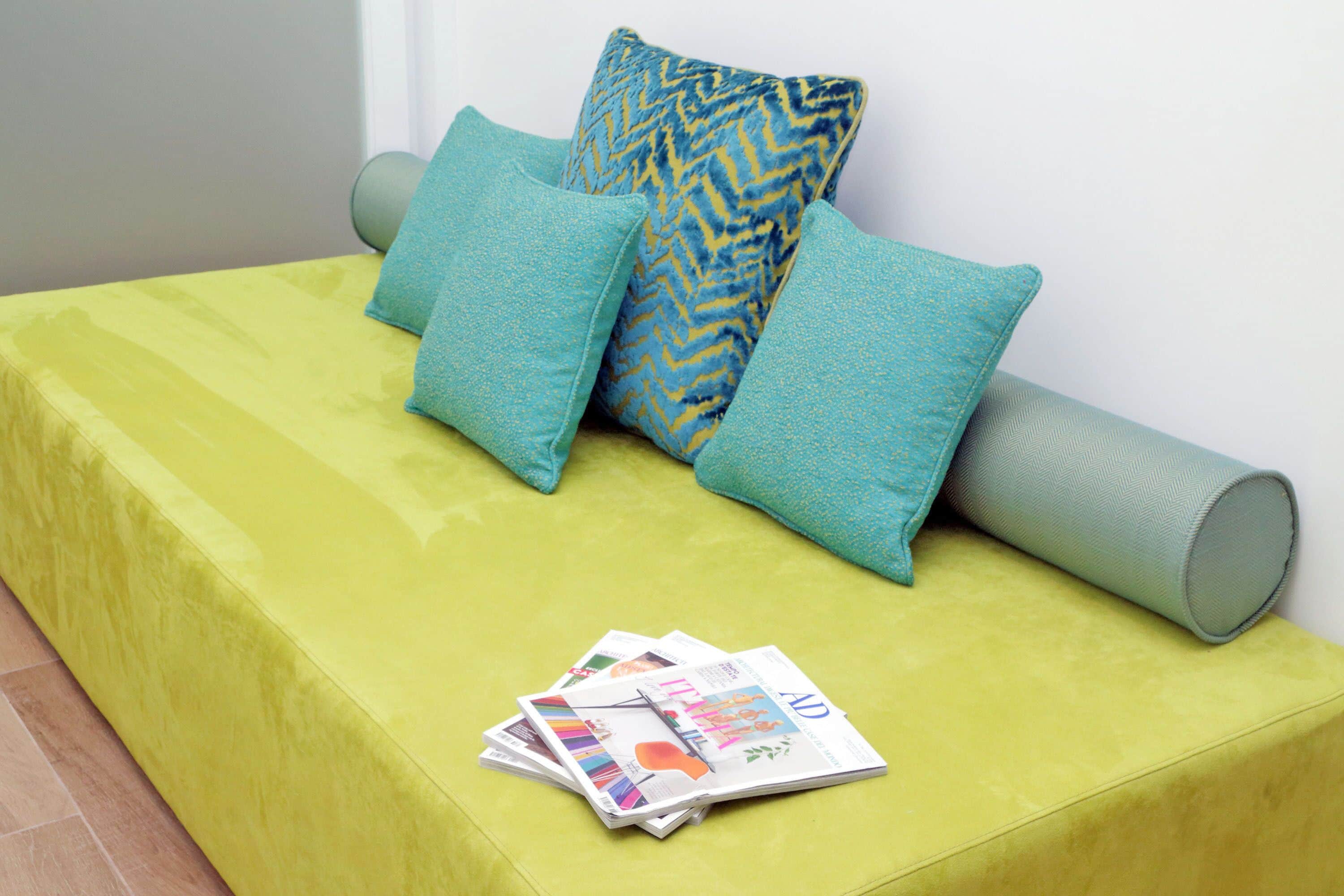 A bright green sofa with patterned cushions and a rolled-up mat, accompanied by a stack of magazines.