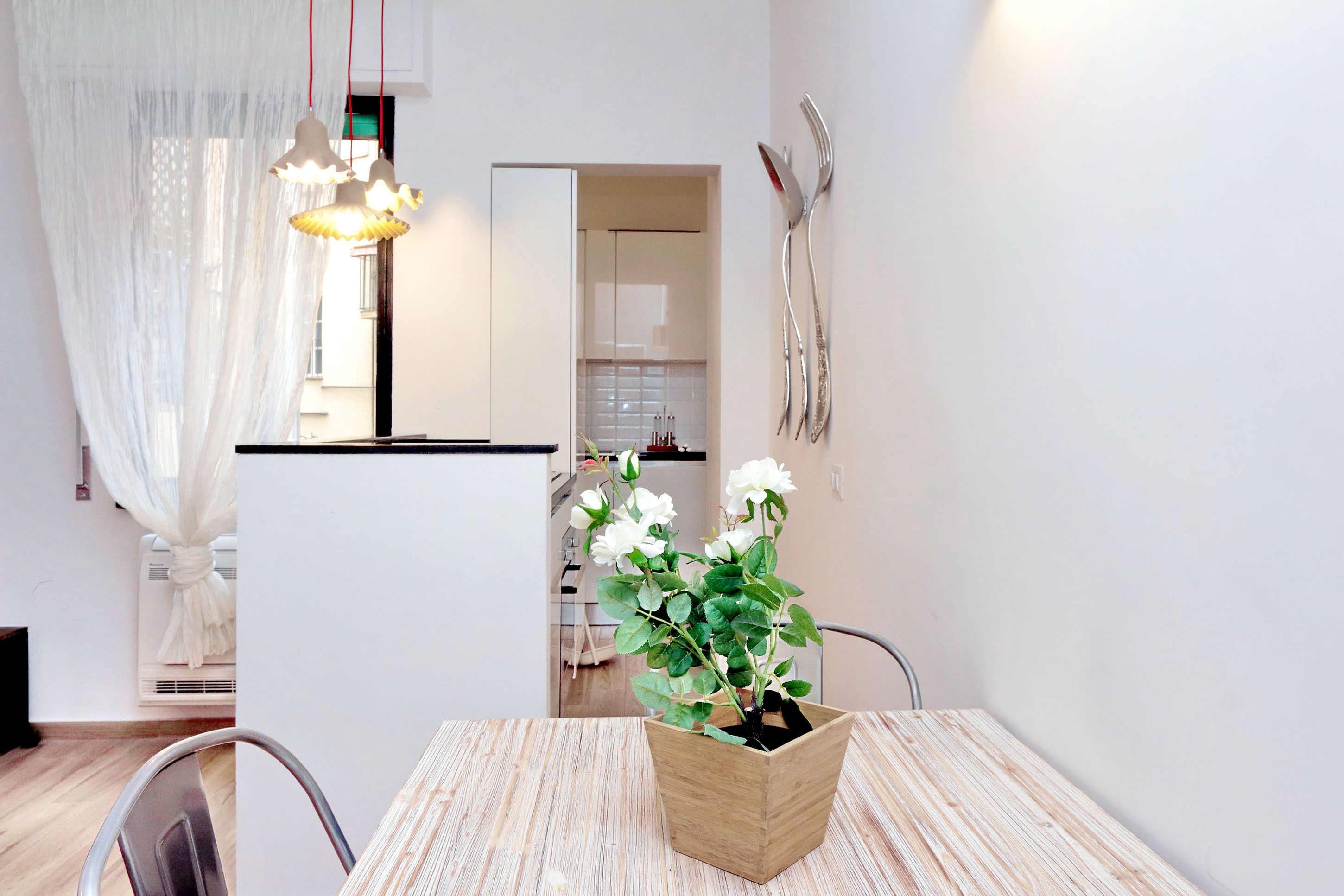 Une cuisine moderne avec des meubles blancs, une table à manger en bois et une plante en pot.