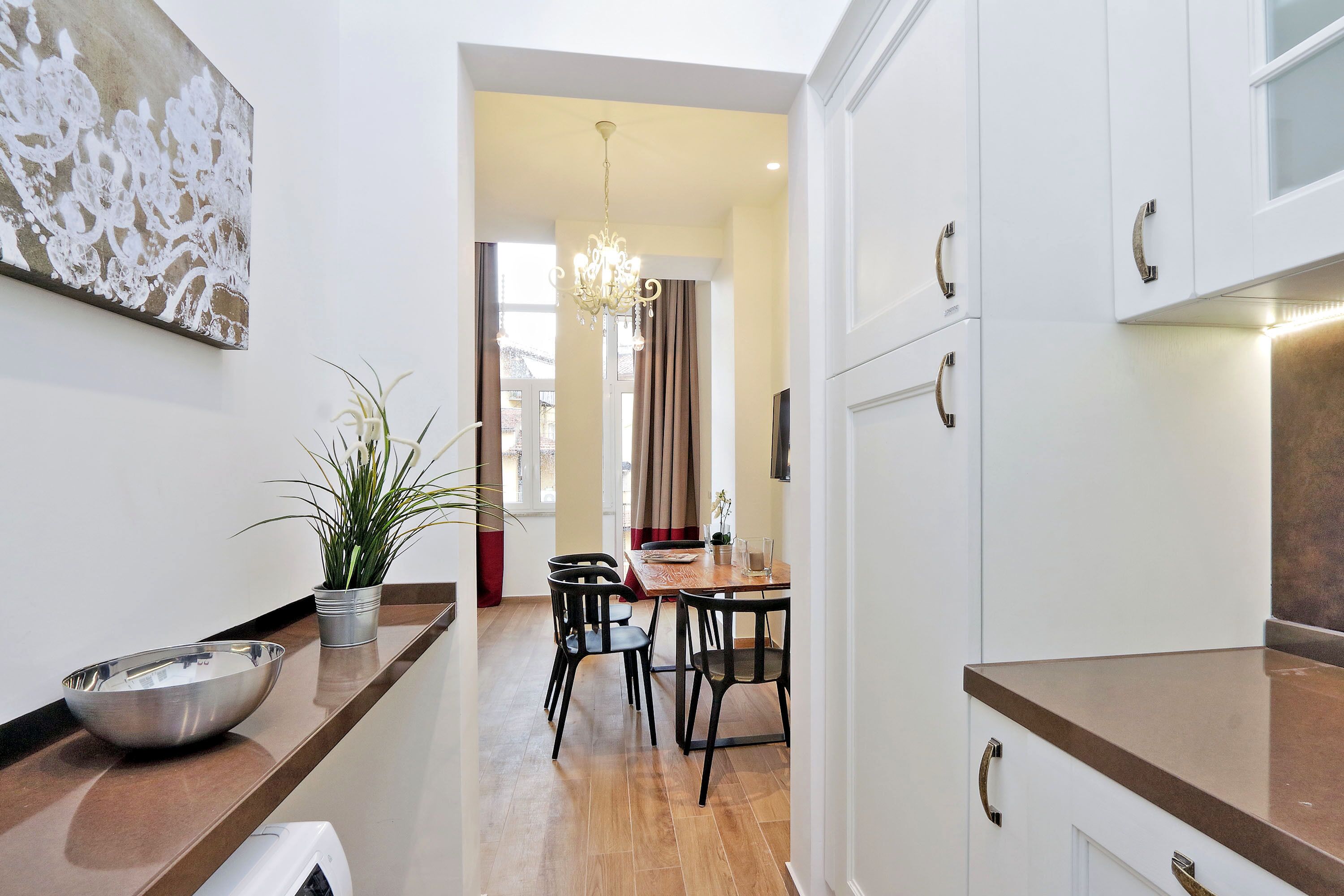 A modern kitchen with a wooden countertop, a dining area with a table and chairs, and a potted plant.