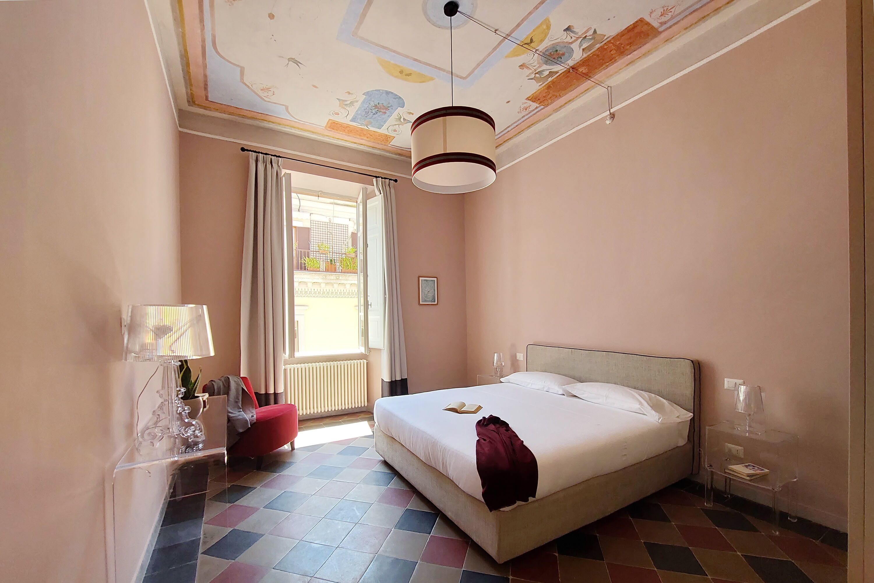 A hotel room with a bed, a nightstand, a lamp, a chair, and a view of the outside.