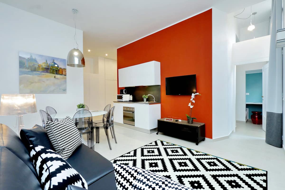 A modern living room with a sofa, patterned rug, and a dining area with chairs and a table.