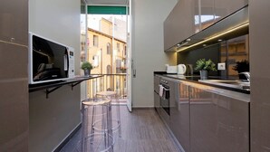 A narrow kitchen with a microwave, a sink, and a small bar area with stools. - Monti Apartments - My Extra Home (Rome)