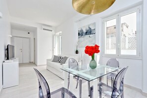 A modern living room with a glass dining table, white sofas, and a large window with a view of buildings. - Monti Apartments - My Extra Home (Rome)